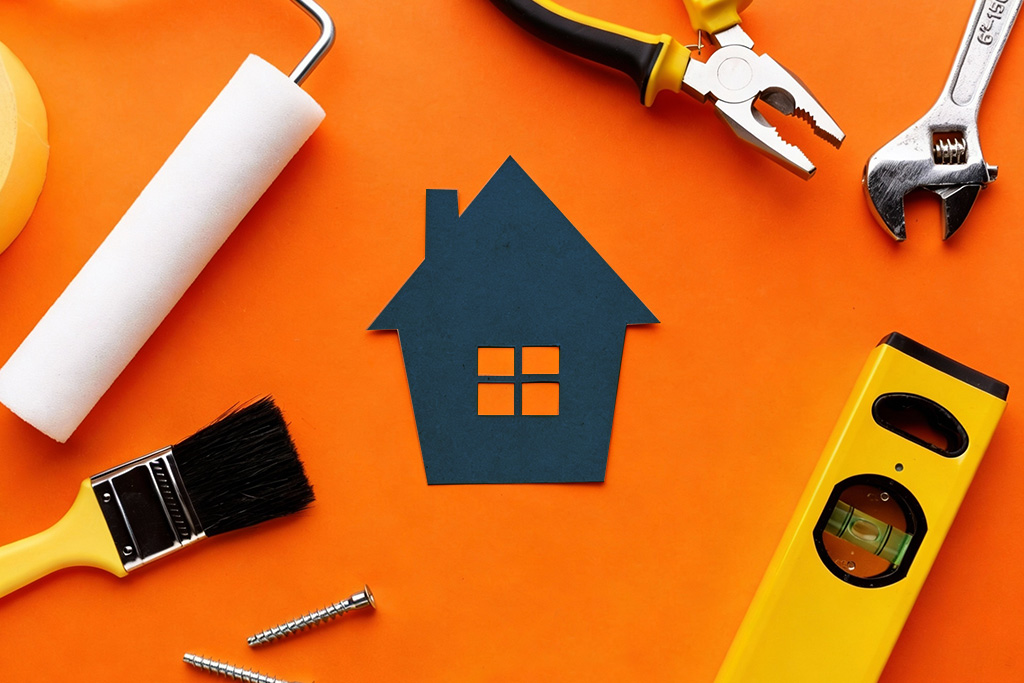 Paint roller, brush, pliers, wrench and level around a paper house